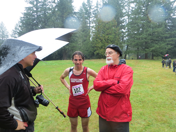 Luke standing with his coaches in the rain on a grassy field with trees in the background.