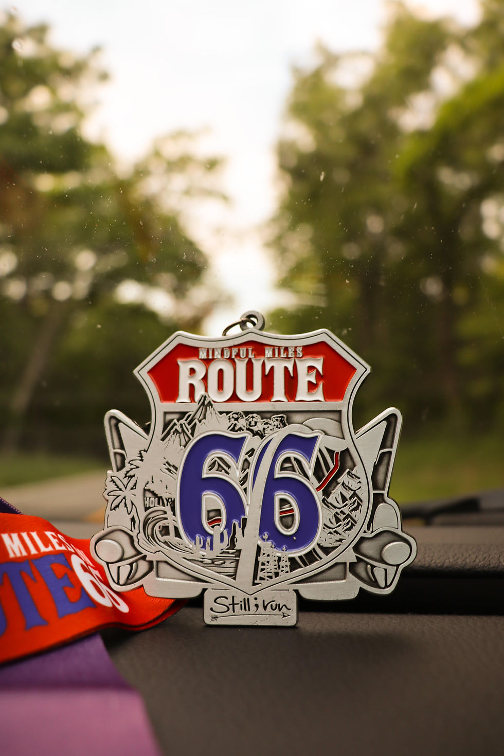 a medal for the Route 66 virtual run challenge sitting on a vehicle dashboard
